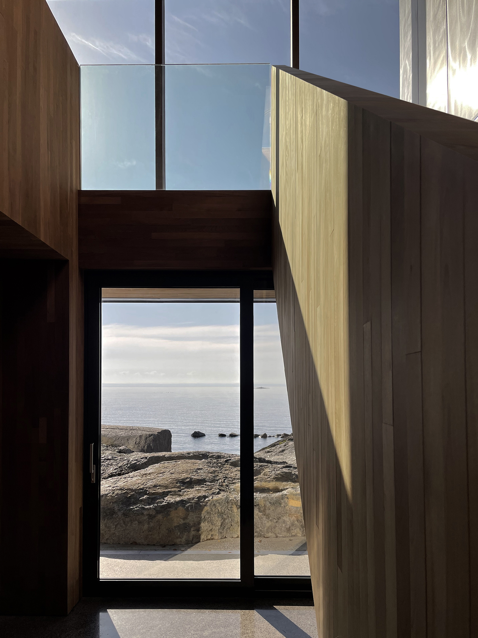 L'intérieur de la résidence faite de bois pâle et de grandes vitres donnant un beau visuel sur la rive d'eau